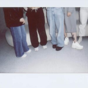 Group of people in casual fashion attire standing indoors, highlighting trendy footwear and denim jeans.
