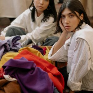 Two women exploring colorful clothes in a thrift store, relaxed and casual setting.